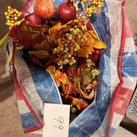 View into bag showing assorted faux fall leaves, berry stems, and faux pomegranates in red and orange colors.