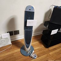 Full view of tower fan standing on wooden floor, power cord coiled at base.