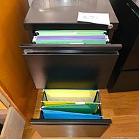 Front and top view of one black two-drawer file cabinet with hanging folders visible inside top and bottom drawers.