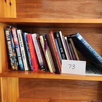 Books placed on wooden shelf showing titles and colorful spines with card labeled '73'.