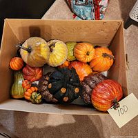 Top down view of cardboard box filled with various faux pumpkins showing glittery gold, black glitter with orange spots, and other colored pumpkins.
