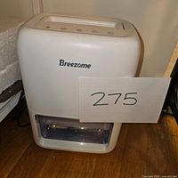 Front view of the Breezome portable dehumidifier showing white body, transparent water tank, and Breezome branding.