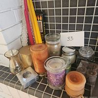 Wide view of assortment of candles and candle holders on a tiled shelf, shows size and color variety