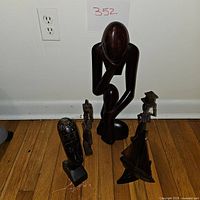 Image showing the four wooden carved sculptures arranged on hardwood floor against a white wall with electrical outlet.