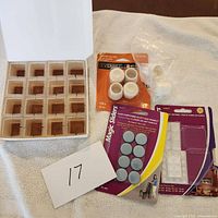 Top-down view of all protectors and sliders arranged on a white towel, including transparent square plastic caps, white round plastic leg protectors, grey felt pads, and white adhesive bumpers.