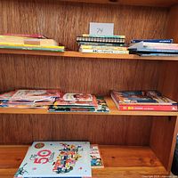 Shelf with various children's books stacked and arranged in piles; includes educational titles and storybooks