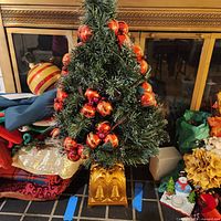Artificial 3 ft Christmas tree decorated with red and gold ball ornaments on decorative gold stand set in front of a fireplace.