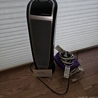 Full view of black and silver ceramic heater alongside purple fan with cords coiled beside it on wooden floor