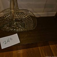 Crystal basket with central handle and diamond-cut pattern placed on wooden surface, photo includes lot number card '240'.