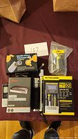 Overview photo of lot items showing HDMI splitter, laser pointer, Nitecore Digi D2 charger, and sealed electronic part.