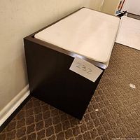 Side perspective showing the dark wood bench with white cushion top and solid construction, minimal design.