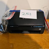 Full view of black Epson printer with power cord in sealed plastic bag, model ES-500W visible on front.