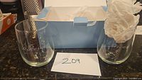 Two clear stemless wine glasses with etched script designs displayed with a light blue box and white tissue paper.