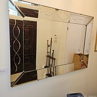 Full view of the large rectangular wall mirror with beveled edges and decorative curved etching on the vertical sides, reflecting an entrance door and hallway.