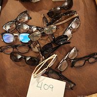 Top view of an assortment of 15 eyeglass readers with various frame styles and colors arranged on a brown surface.