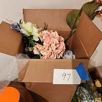 Photo of a cardboard box containing an assortment of faux flowers featuring hydrangeas in several colors and other floral stems.