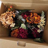Box filled with various faux flowers in mixed colors including beige, light orange, burgundy, dark red, and cream hydrangea, snapdragons, and orchids.