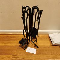 Full view of the complete set of black metal fireplace tools on the stand, showing all components arranged upright.