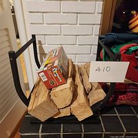Black metal fireplace wood holder with curved base, holding several wood logs and a fire starter box, presumably for stage display.