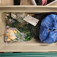 Plastic bin containing artificial flowers in bags, chicken wire, and green floral stems.