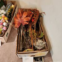 Box containing various wooden stems, large brown leaves, orange and red artificial berries, and other floral display extras