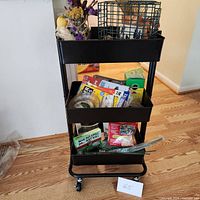 Full view of garden plant cart showing three black metal trays on wheels loaded with various gardening supplies and dried flowers