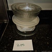 Four clear ribbed glass bowls stacked, with white plastic lid on one.
