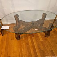 Top view of oval glass coffee table showing carved wooden base details and glass thickness.