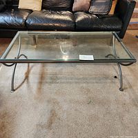 Photo of the rectangular glass coffee table with brushed chrome frame and legs, seen from above showing the top and partial view of black couch in background.