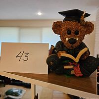 Side view of the ceramic graduation bear figurine sitting on a wooden surface with a note card labeled '43' beside it.
