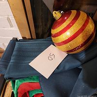 Large red and gold glitter striped Christmas ball ornament resting on folded dark blue tablecloth.