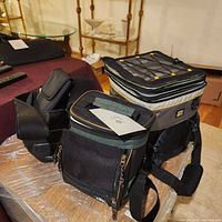 Three insulated tote bags shown on a table, one large grey and black Thermos cooler bag and two smaller black insulated totes