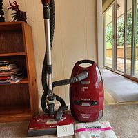 Kenmore Intuition vacuum cleaner overall view with flexible hose, wand, and filter bag on carpet near wooden furniture and glass door.