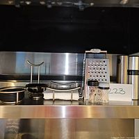 Photo showing box grater, metal trivet, two small spice containers and part of a pepper mill