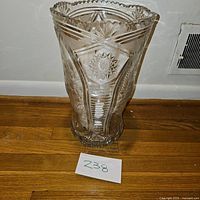 Front view of large clear cut glass vase with detailed patterns on a wooden floor.