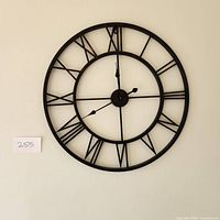 Large black metal wall clock with Roman numerals hanging on a light-colored wall, 30 inch wide size.