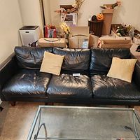 Full view of black leather couch with two beige cushions showing overall condition and setup in room.