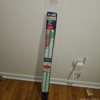 View of two rolled maps packaged together in original retail box leaning against a wall on floor, showing partial map colors.