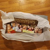 Wooden Memories photo frame new in box wrapped in white tissue paper, showing its design with multiple clips to hold photos.