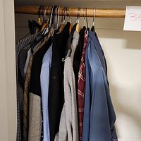 Photo showing a selection of men's shirts on hangers on a wooden rod including various colors and styles.