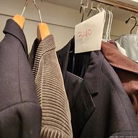 Photo of men's jackets hanging on wooden hangers including two suit jackets, corduroy jacket, brown jacket, white shirt, plaid jacket
