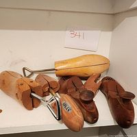 Three pairs of men's wooden shoe trees placed on a white shelf, showing different wood tones and metal hardware.