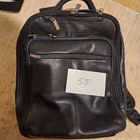 Front view of the black leather messenger backpack with multiple zippered compartments and top handle