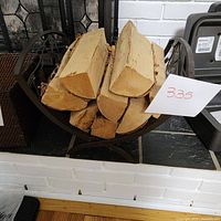 Black metal decorative wood holder positioned with firewood inside (firewood not included).