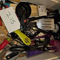 Top view of miscellaneous kitchen utensils including measuring cups, spatula, tongs, whisk, jar opener, and bamboo skewers.