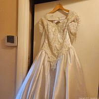 Front view of full white wedding gown showing bodice with intricate beadwork and puff sleeves, and voluminous satin skirt.
