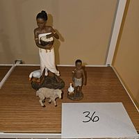 Four nativity figurines including woman, boy, sheep, and geese on wooden surface.