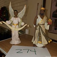 Photo showing two nativity figurines, an angel, and a king on a wooden surface.