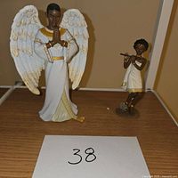 Two nativity figurines on display: one angel with white wings, gold detailing and praying pose, other smaller angel playing flute.