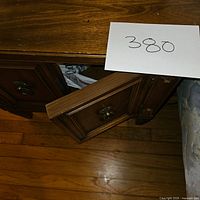 Close-up of top and front corner of nightstand with partially open cabinet door, showing wood grain and brass ring pull handle.